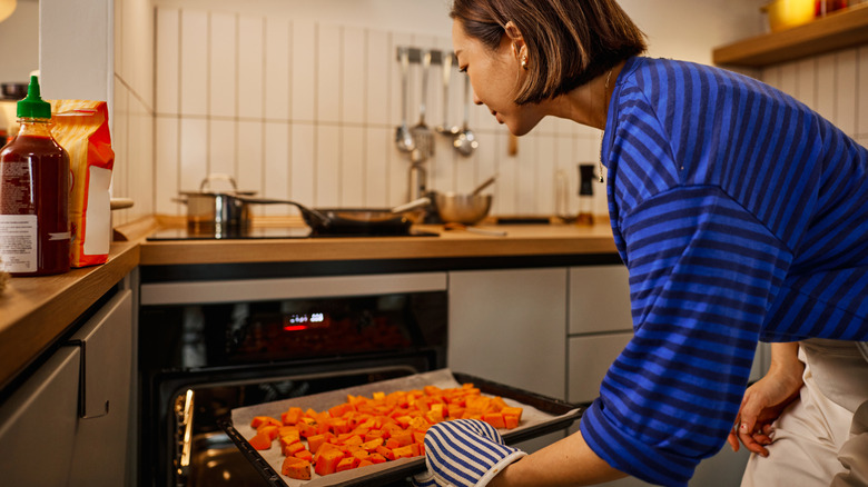A woman places a tray of cubed squash into an oven