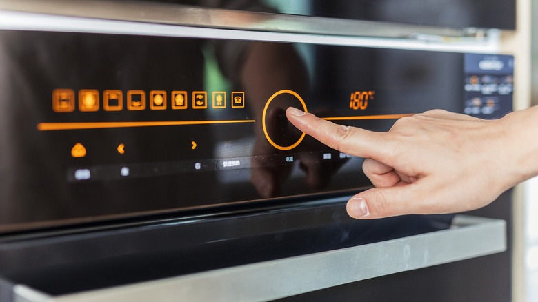 Person's hand setting temperature on an oven.