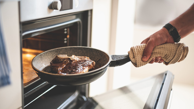 Hand holding a pan near an oven