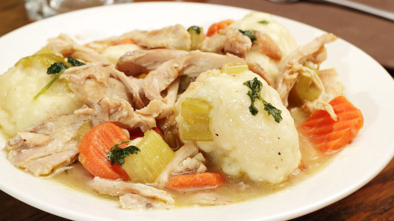 White plate filled with chicken and dumplings in gravy with chunks of carrot and celery