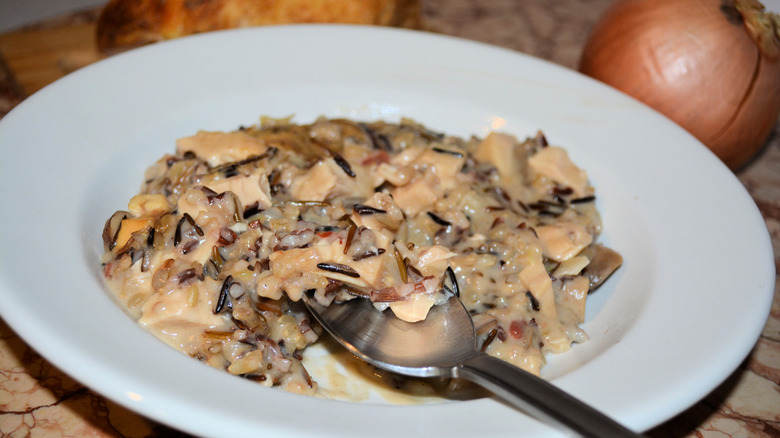 Closeup shot of a bowl of chicken and wild rice casserole with a spoon dipped in for a bite, and an onion sits behind it