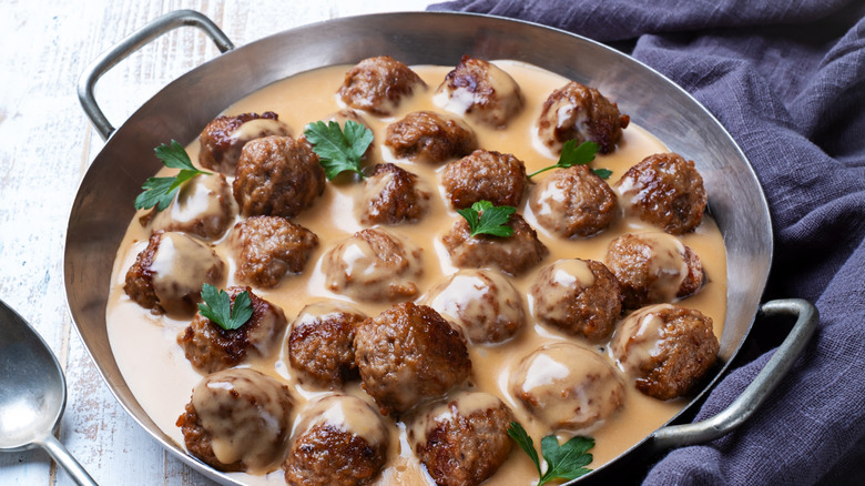 Metal round skillet filled with Swedish meatballs in creamy gravy topped with sprigs of parsley