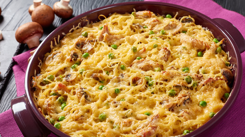 Round casserole dish filled with turkey tetrazzini, made with spaghetti noodles, on a cloth napkin on a table with mushrooms in the background
