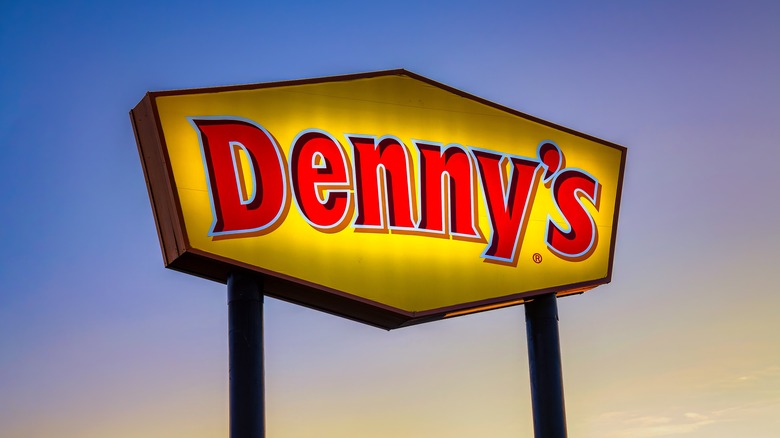 Denny's sign lit up as the sun rises in the background