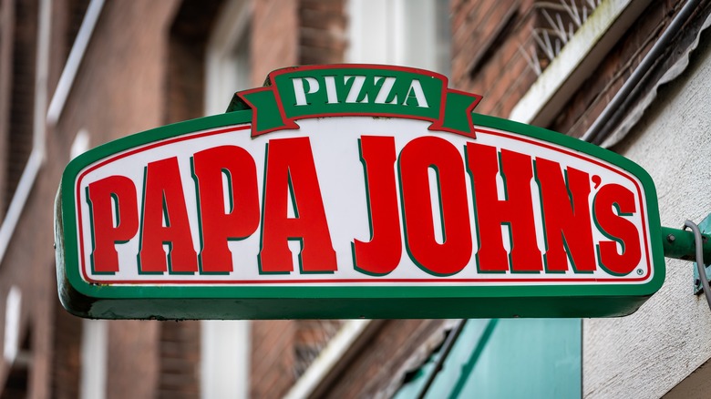 Papa John's Pizza sign juts out from a wall in an urban area