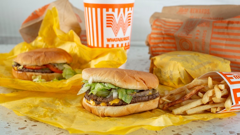 Whataburger sandwiches, fries, and a drink arranged with takeout bags