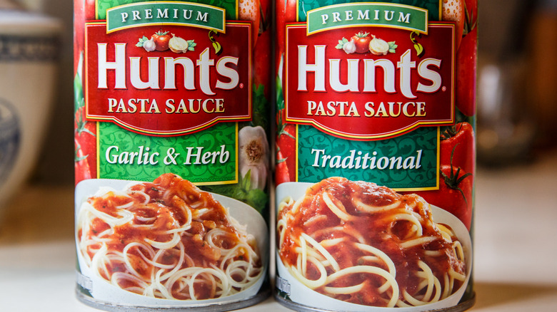 Two large cans of Hunt's brand premium Pasta Sauce in Garlic & Herb and Traditional flavors
