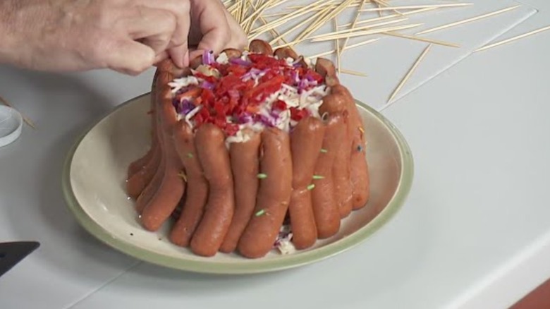 A person assembling a crown roast of frankfurters with toothpicks.