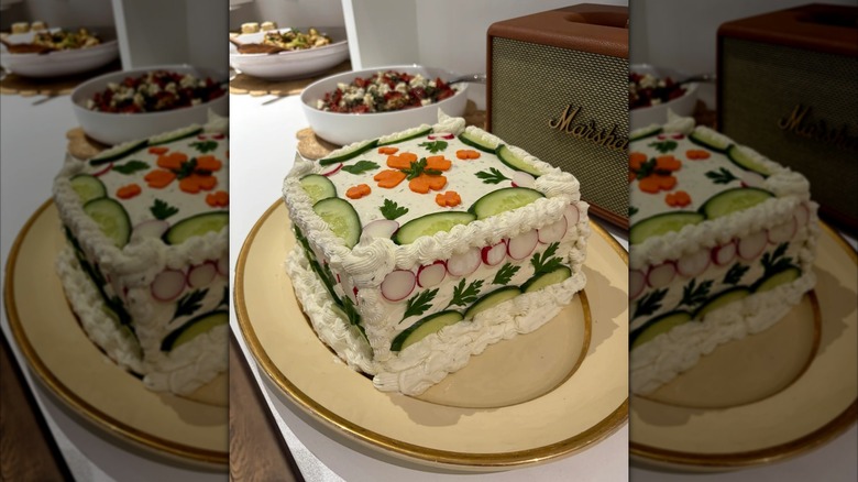 A frosted sandwich loaf decorated with cucumber and carrot slices.