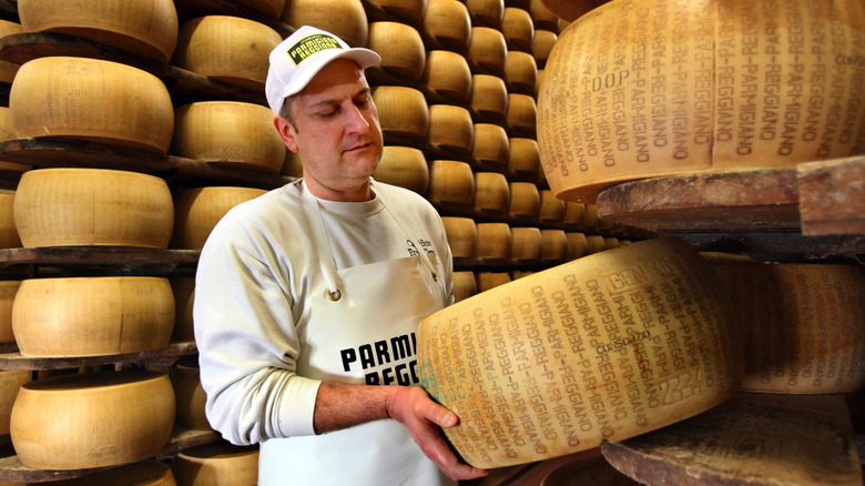 man lifting a wheel of Parmigiano-Reggiano with many other wheels on shelves nearby