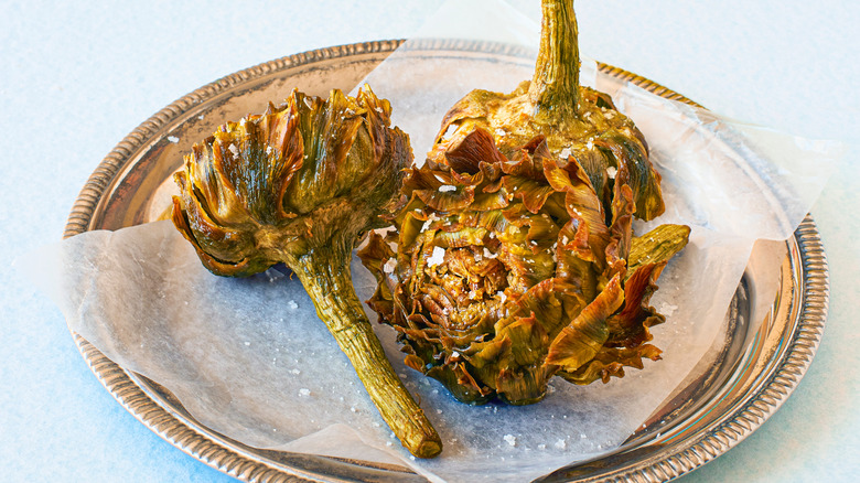 Roman deep-fried artichokes sprinkled with salt on paper on a silver tray