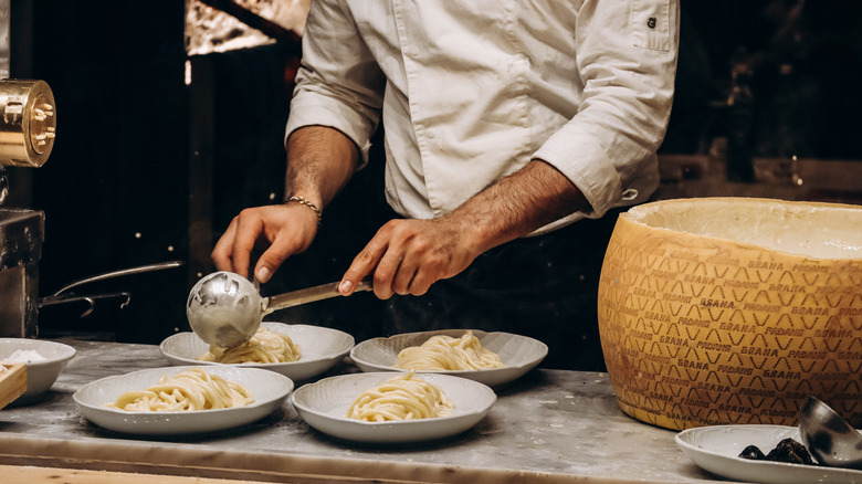 chef plating creamy pasta with wheel of grana padano on the side