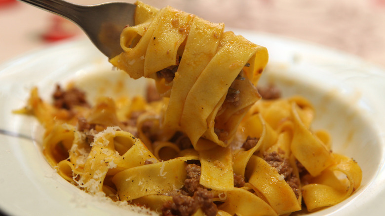 close up of pappardelle wound around a fork with meat sauce and grated cheese