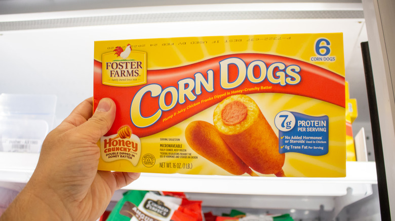 Box of corn dogs held in front of an open freezer