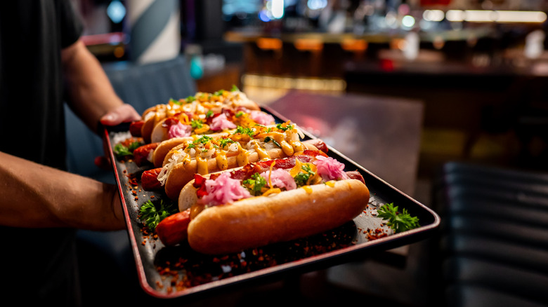 Garnished hot dogs on a waiter's tray near a booth
