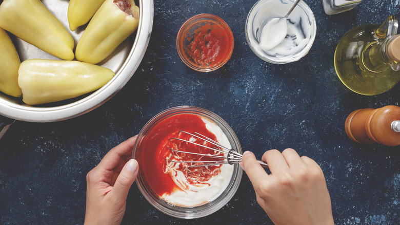 Hands mixing tomato sauce and sour cream for stuffed bell peppers