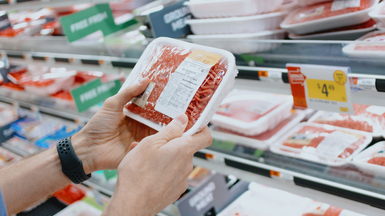 Hands holding package of ground meat in grocery store