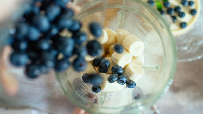 bananas slices in a blender with blueberries being added.