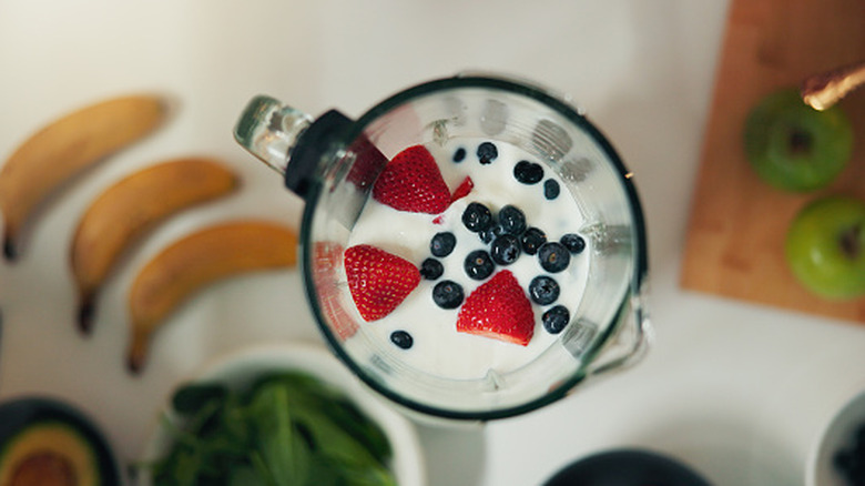 a blender jar filled with milk, strawberries, and blueberries.