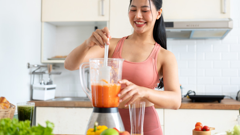 a young woman scraping the inside of her blender jar with a white spatula.