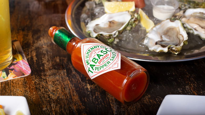 Bottle of Tabasco sauce next to a plate of oysters.