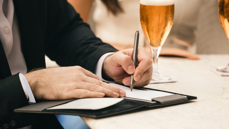 Person signing the bill at a restaurant with a pen.