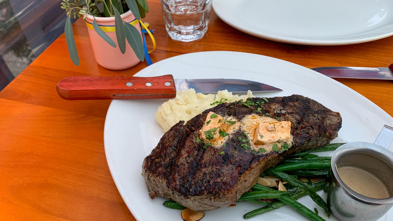 Steak knife on a plate next to a steak, green beans, and potatoes.