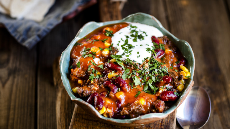 Bowl of chili with beans topped with sour cream and herbs plated on a planked wooden table