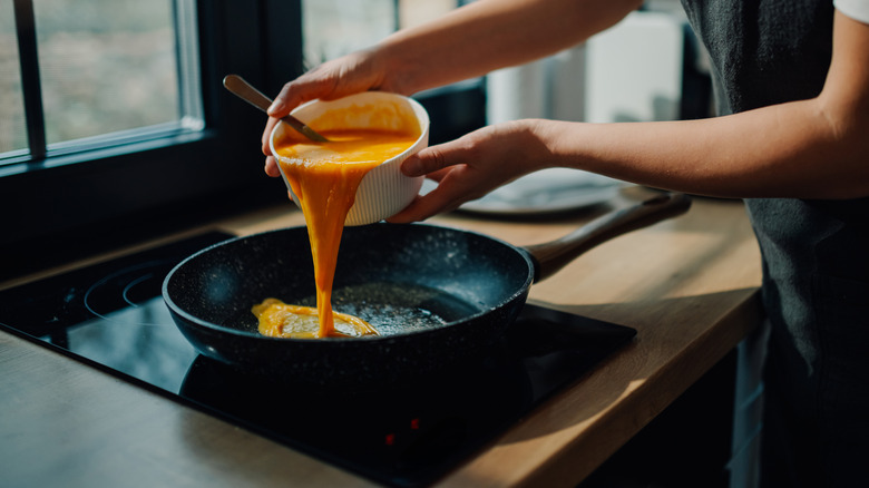 Person pouring bowl of whisked eggs into a pan