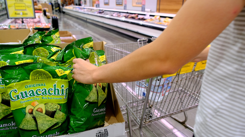 hand grabbing a bag of el sabroso guacachips next to a shopping cart