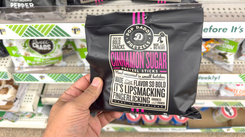 a hand holding a small bag of pop daddy cinnamon sugar pretzel sticks in front of a store shelf
