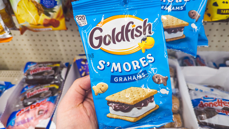 a hand holding a bag of goldfish grahams s'mores in front of a store shelf