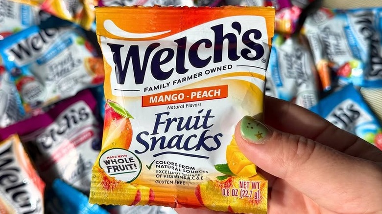 a hand holding a bag of welch's mango-peach fruit snacks