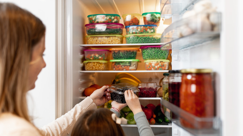mother daughter taking out containers from refrigerator
