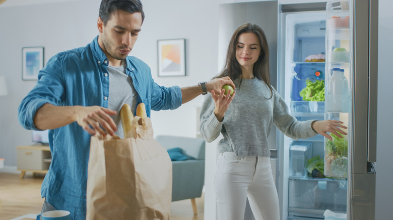couple stock groceries in refrigerator