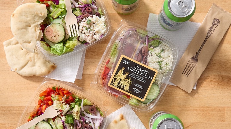 Three packages of Trader Joe's Classic Greek Salad with pita and canned drinks