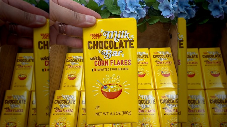 A Trader Joe's Milk Chocolate Bar with Corn Flakes held over a display of the chocolate