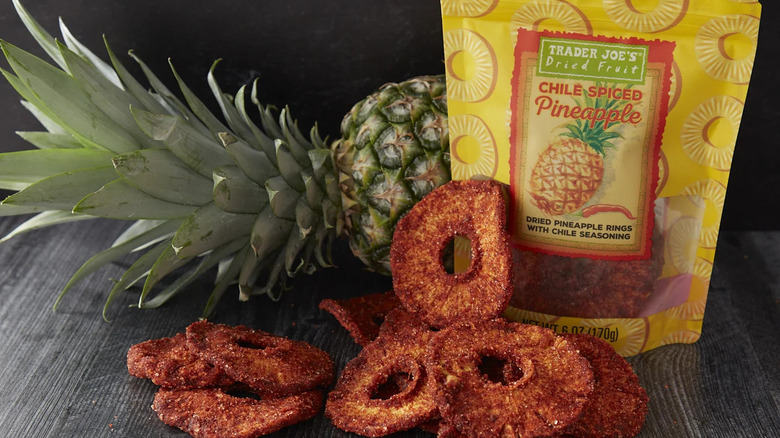 A bag of Trader Joe's Chile Spiced Pineapple next to some of the spicy-sweet pineapple rings and a whole pineapple
