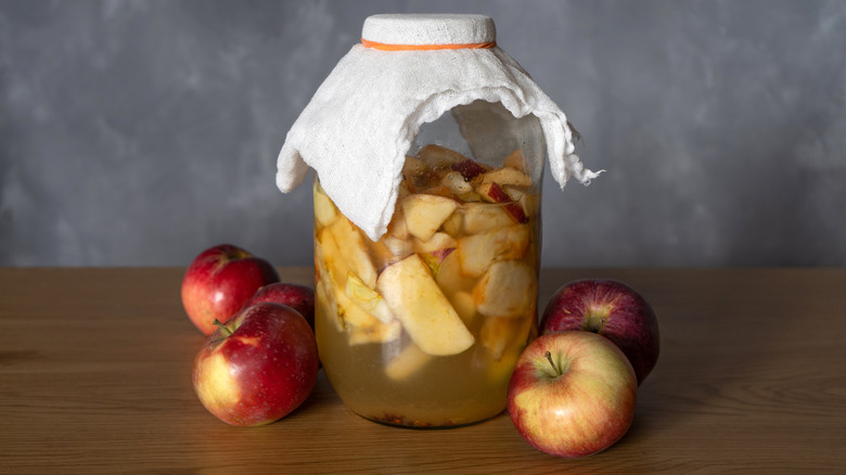 jar of homemade apple cider vinegar with whole apples alongside