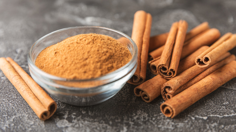 Cinnamon sticks and grounded cinnamon in a glass bowl.
