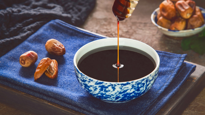 A blue bowl of date syrup with some fresh dates on the side.