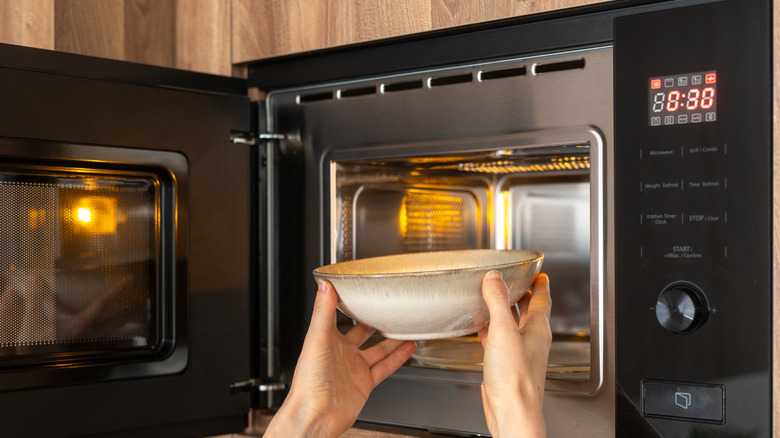 Hands placing a ceramic bowl in a microwave