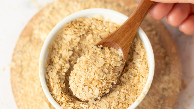 Hand scooping nutritional yeast out of container with a wooden spoon