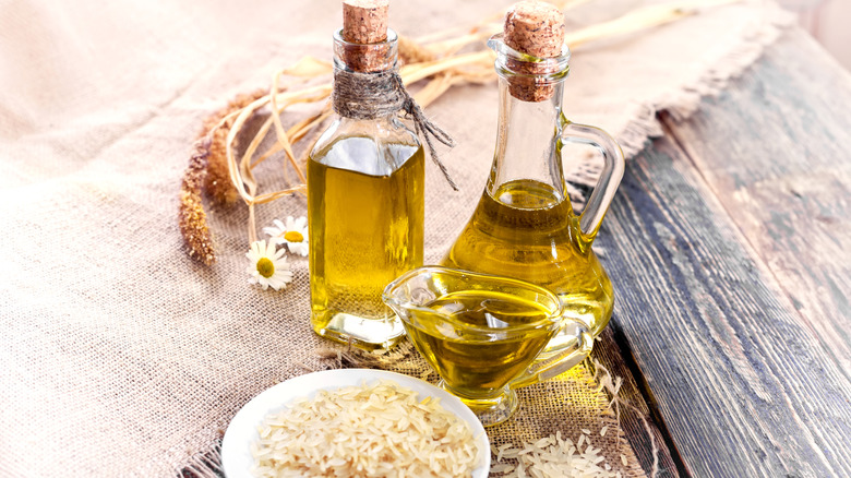 Two bottles of oil set next to a pile of rice on a wooden table