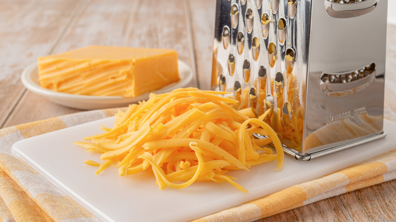 Freshly shredded cheddar cheese on cutting board with grater