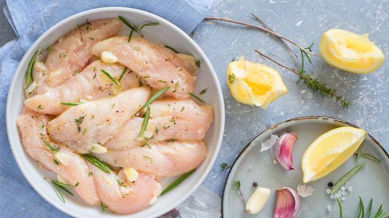 Chicken marinating in a bowl with herbs, lemon, and garlic