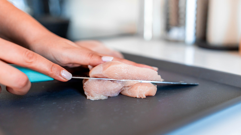 Person slicing raw chicken on a cutting board