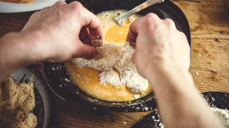 hands holding chicken tender in egg wash