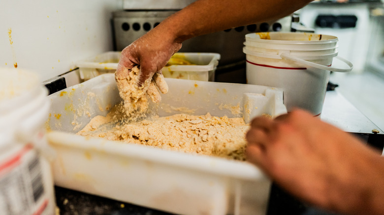 Hands breading chicken in plastic container