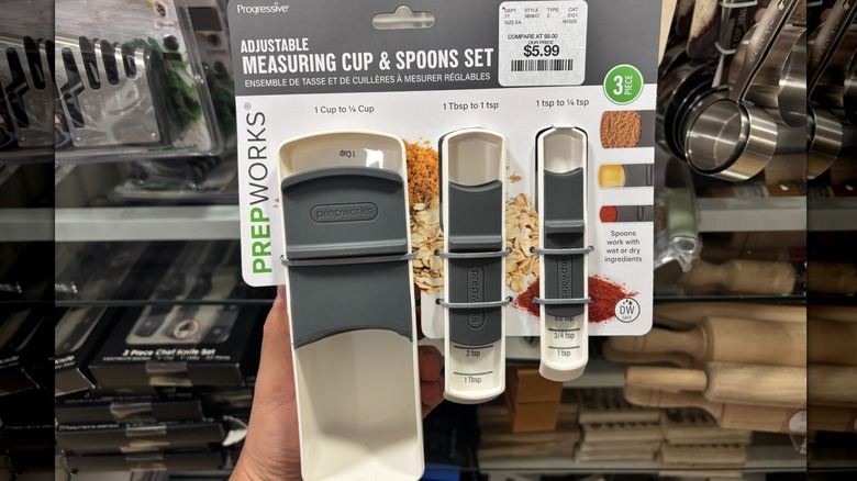 A person is holding a three piece measuring spoon set in a store.
